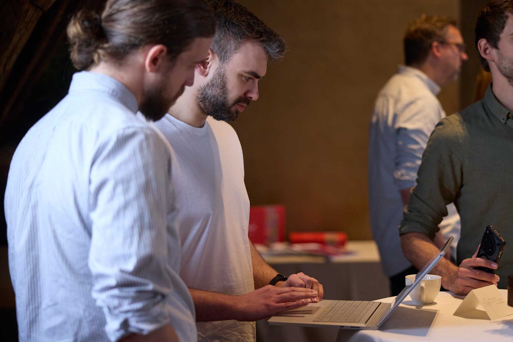 Drie personen bespreken informatie rond een laptop tijdens een professioneel netwerkevent.